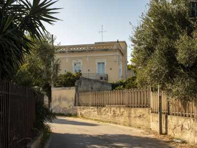 Appena immessi nella via ci ritroviamo subito di fronte a due antiche ville che si ergono oltre i loro muri perimetrali. Una di queste ci appare con un prospetto ocra scandito da tre finestroni sormontati da una balaustra che ne delimita il terrazzo